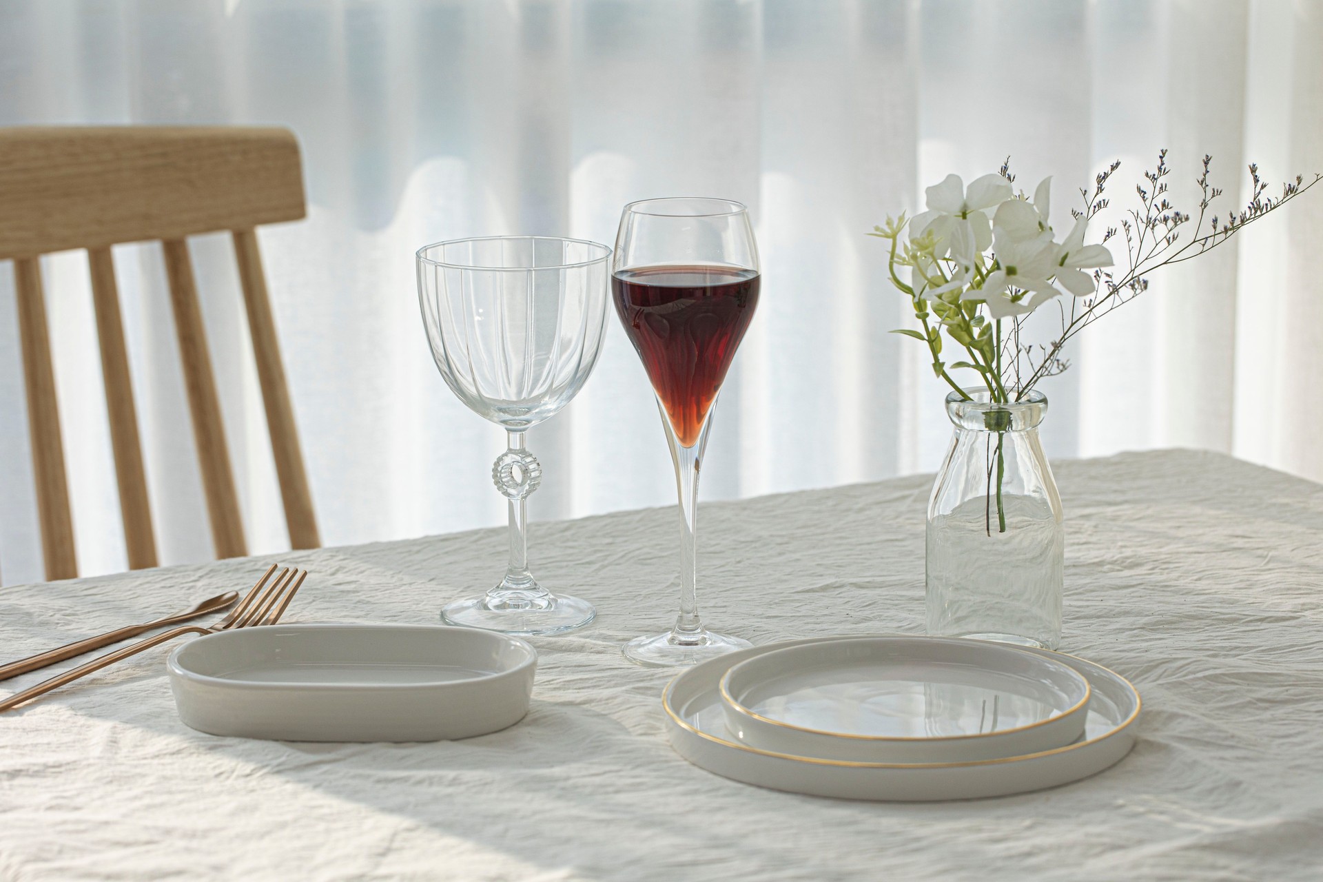 Wine glasses and white plates on white table.