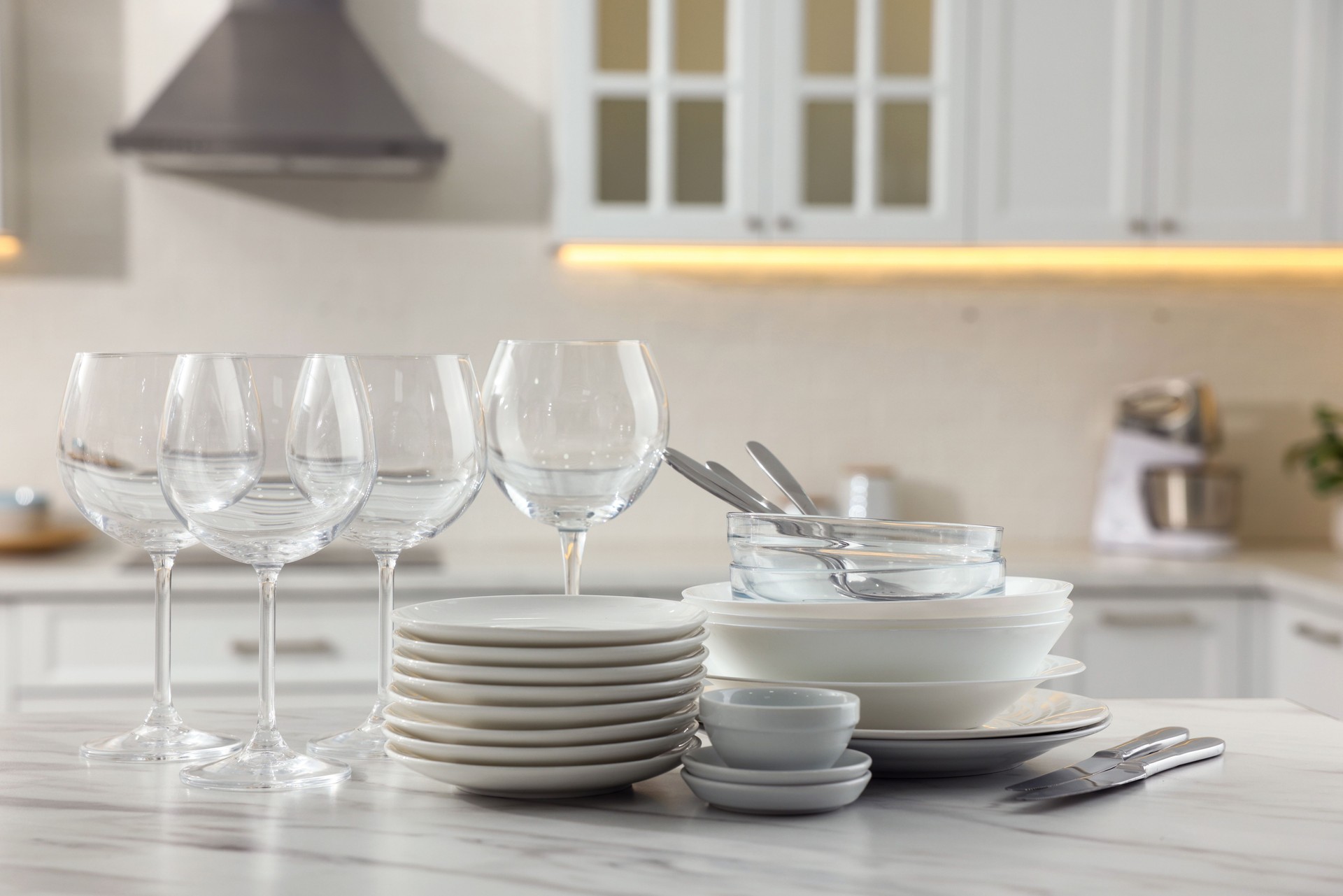 Different clean dishware, cutlery and glasses on white marble table in kitchen
